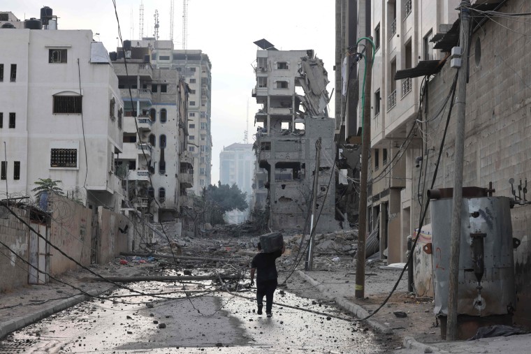 A Palestinian man walks past damaged buildings with a suitcase on his shoulders following Israeli airstrikes in Gaza City