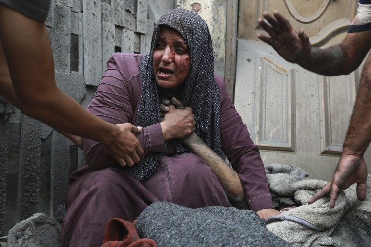 A wounded Palestinian woman cries as she holds the hand of her dead relative outside her home following Israeli airstrikes in their neighborhood in Gaza City, Monday, Oct. 23, 2023. 