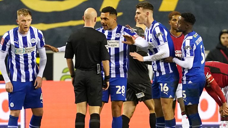 The Wigan players surround Anthony Taylor