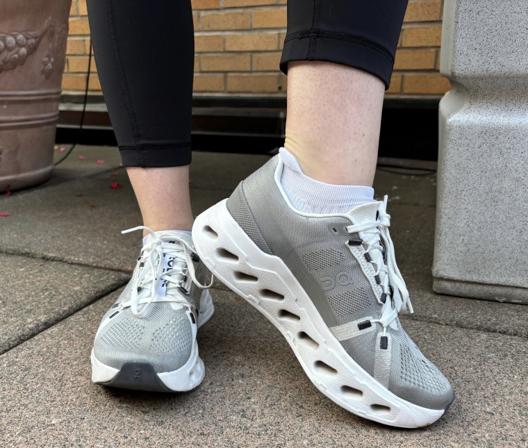 Woman's feet wearing grey and white On Cloudeclipse sneakers while standing outside.